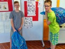 2 Schüler halten zwei Säcke, voll mit Deckeln.