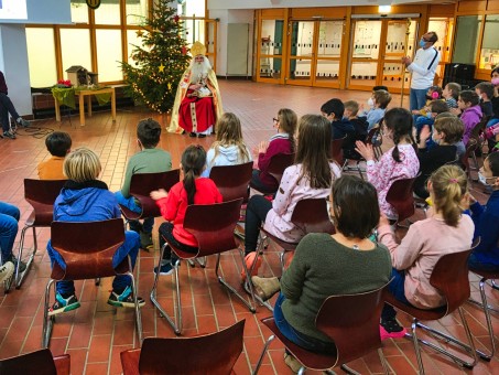 Bild vom Nikolaus. Vor ihm sitzen viele Schüler*innen in einem Halbkreis. Der Nikolaus spricht zu den Schüler*innen.