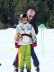 Bild von 2 Personen auf Skiern. Eine Lehrerin steht hinter einer Schülerin und unterstützt diese.