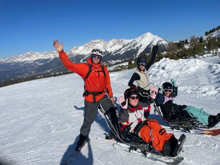 Bild von 2 Schülern in einem Gerät auf der Piste. Hinter ihnen stehen 2 Begleiter.