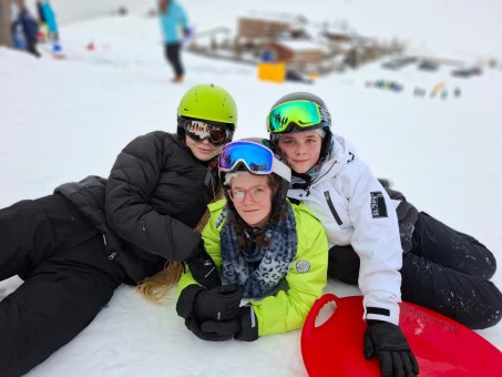 Bild von 3 Schülerinnen, die auf der Skipiste sitzen.