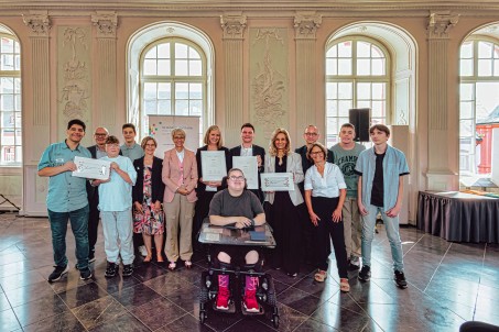 Gruppenbild von 14 Personen. Zwei Personen halten eine Urkunde.
