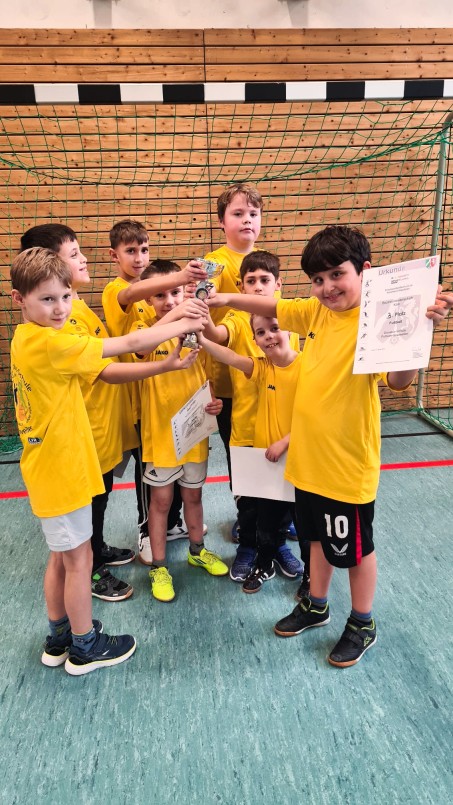 Bild von 8 Sch&uuml;lern in einem Trikot. Sie halten einen Pokal in der Mitte hoch.