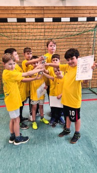 Bild von 8 Sch&uuml;lern in einem Trikot. Sie halten einen Pokal in der Mitte hoch.